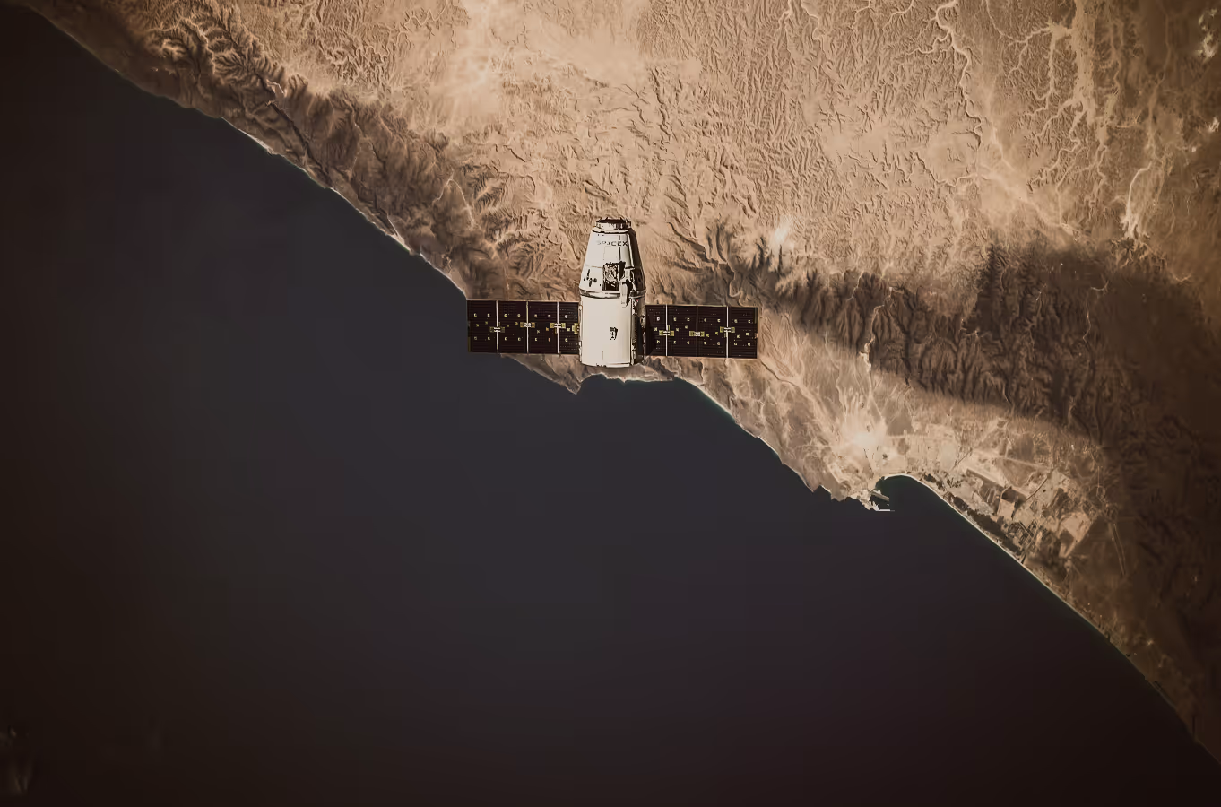 SpaceX satellite orbiting above a coastline with desert terrain and ocean visible below.